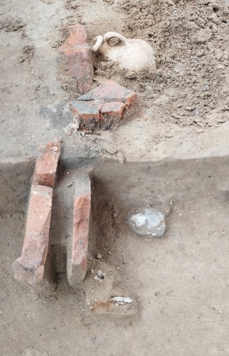 (c) Martha Aeissen / ARCHAEOnet
Nahaufnahme zweier halb ausgegrabener Relikte. Während die Form im Vordergrund an eine Mauer erinnert, ist das Relikt im Hintergrund als Krug oder Kanne erkennbar.