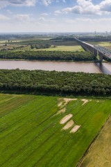 Landschaftsbild: EIne Brücke führt über Feld und Fluss.