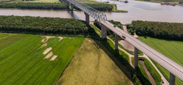Landschaftsbild: EIne Brücke führt über Feld und Fluss.
